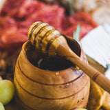 Olive wood honey dipper with honey dripping from it into a wood honey pot