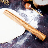 Large wooden dowel shaped rollig pin on a dark surface with pie crust rolled out