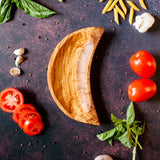 Wooden dish shaped like a crescent moon on a dark background with cooking ingredients