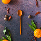 Carved wooden dip spoon on a dark background with oranges, greenery and red chili peppers