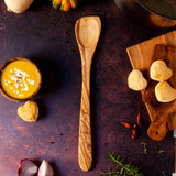 Pointed wooded spoon with extra long handle on dark background with butternut squash soup and heart shaped biscuits