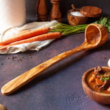 Extra long olive wood ladle on a dark background with carrots and a bowl of stew
