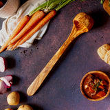 Extra long olive wood ladle on a dark background with carrots and a bowl of stew