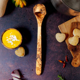 Extra long wooden ladle on a dark background with butternut squash soup and heart biscuits.