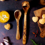 Two sizes of wooden ladles on a dark background with butternut squash soup and heart biscuits.