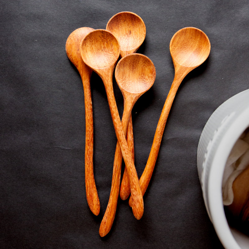 pile of five hand carved curvy wooden spoons on a black background