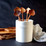 Five aspen leaf shaped spoons in a white utensil crock on a dark background
