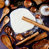 lots of wooden and copper utensils on a dark background with dough