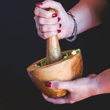 Two hands smashing an avocado in a wooden mortar & pestle