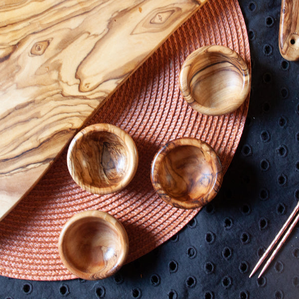 Four small olive wood pinch bowls on an orange and black background