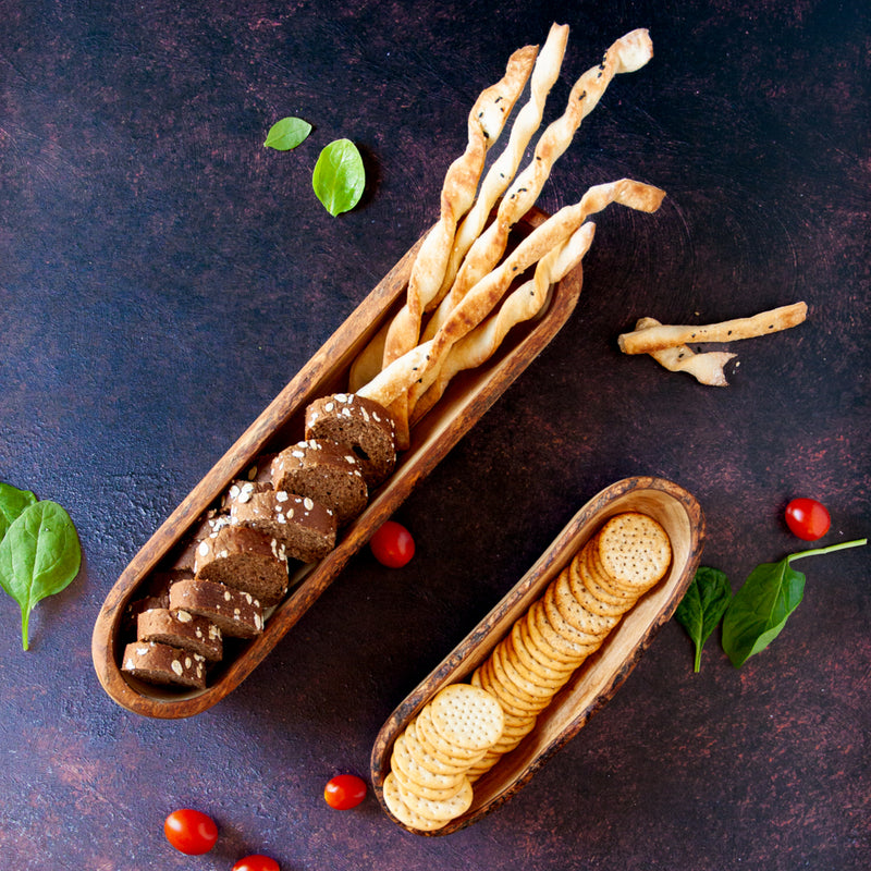 Large wooden bread basket with smaller wooden cracker basket filled with crackers, bread and grissini on a dark background