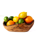 A rustic wooden bowl filled with citrus fruits, including lemons, oranges, and limes, photographed on a clean white background.