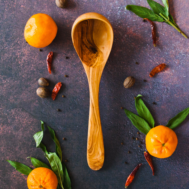 Olive wood soup ladle on a rusty dark background with oranges, leaves and chili peppers surrounding it