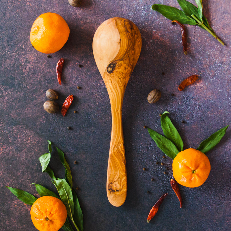 Bottom side up soup ladle on dark background with clementines, greenery and red chilis
