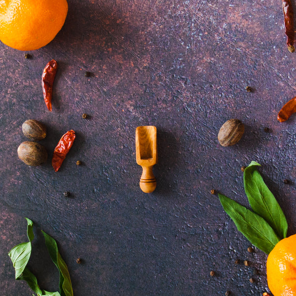 Small wooden scoop on dark background surrounded by oranges, leaves and chilis