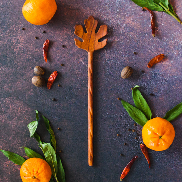 Oak Leaf shaped spoon on a rusty dark background with oranges, green leaves and red chilis
