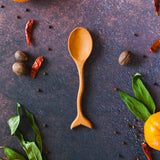 Wooden spoon with a fish tail and wavy handle on a rusty dark surface with oranges, greenery and red chilis