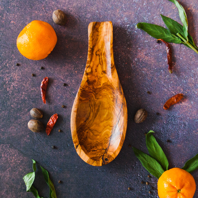 Olive wood spoon holder on a dark surface with oranges, leaves and peppers