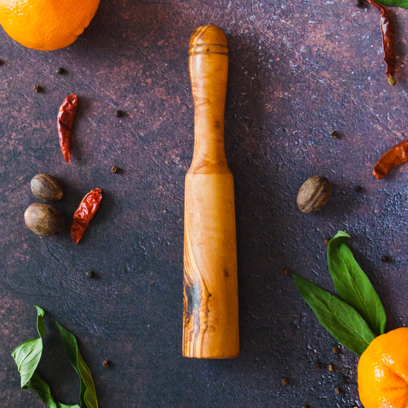 Olive wood drink muddler on a rusty dark surface with clementines, green leaves and red chilis