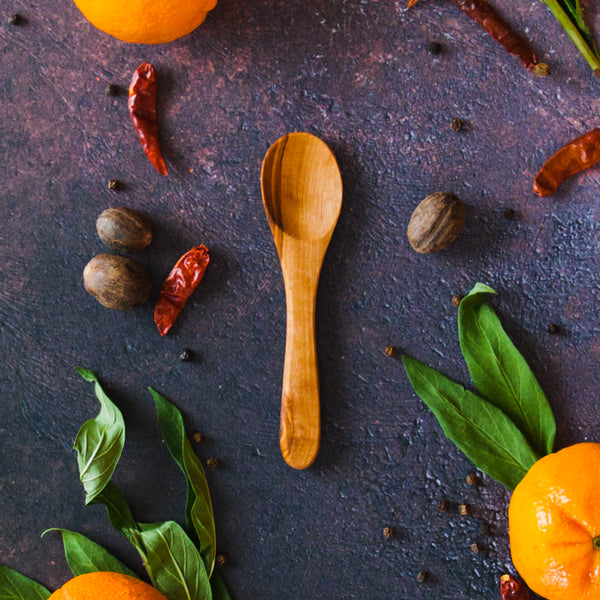 Olive wood appetizer spoon on a rusty dark surface with clementines, green leaves and red chilis around it