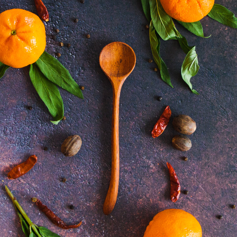 Curvy wooden spoon on a black rusty background with oranges, greenery, and red peppers