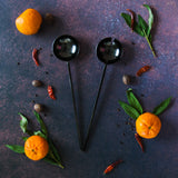 Gunmetal black salad servers on dark background with oranges, green leaves and red chilis