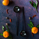 Set of two black metal salad servers on a rusty dark background with cuties, green leaves and red chili peppers