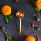 Copper coffee scoop with a gold handle on a dark background with oranges, leaves and red peppers