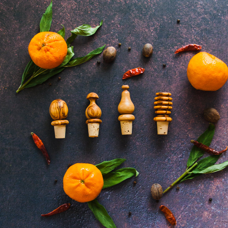 Four olive wood bottle stoppers on dark surface with clementines, leaves and red chilis