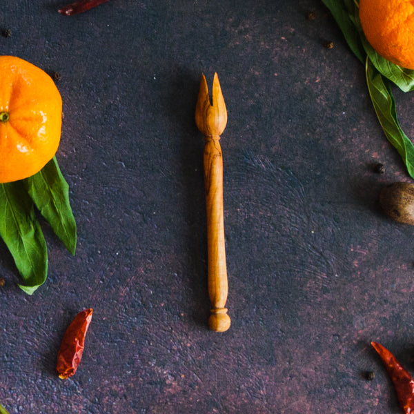 Olive wood pickle fork on a dark rusty background with oranges, greenery and red chilis