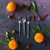 silver appetizer fork, coffee spoon and cheese knife on a rusty background with oranges, greens and red peppers