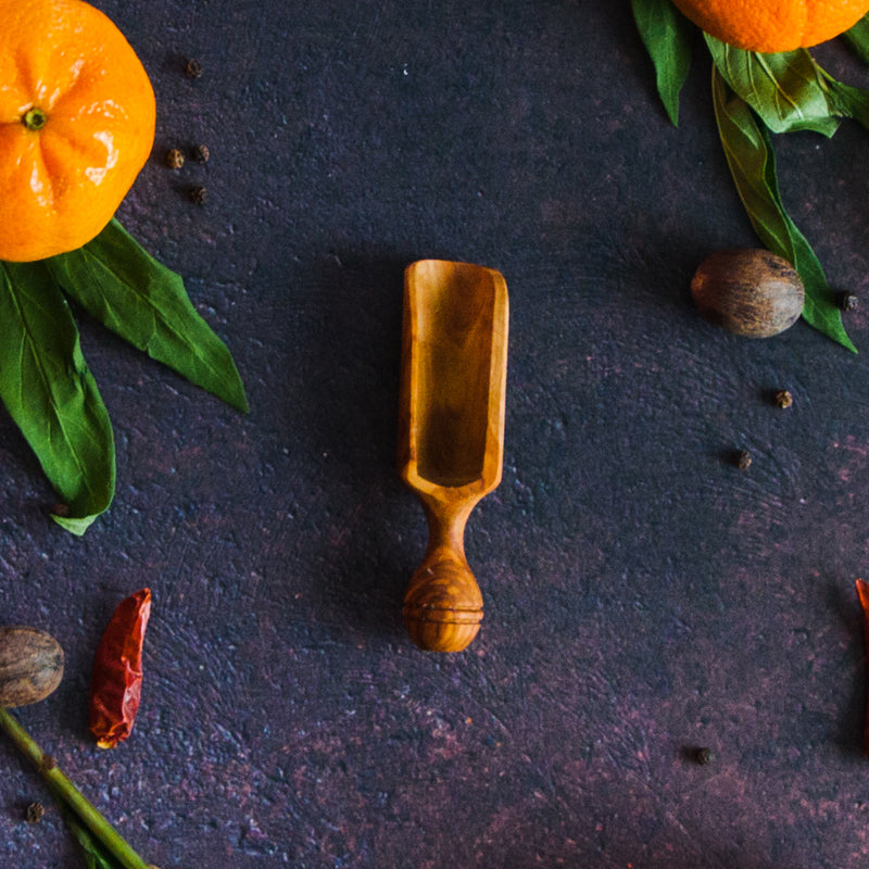 Medium wood scoop on a rusty surface with oranges, leaves and red pepper