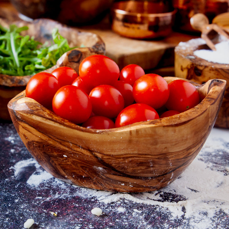 live edge wooden dish filled with cherry tomatoes on a dark background dusted with flour