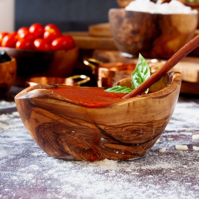 small wooden boat filled with tomato sauce, paired with a spoon on a flour dusted background