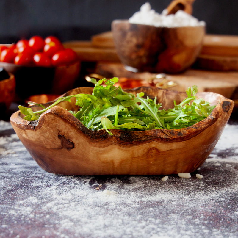 Live edge wooden dish filled with arugula on a flour dusted background