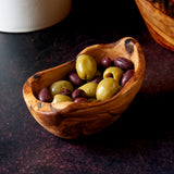 small rustic olive wood dish filled with olives on a dark background