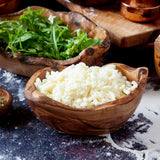 small raw edge bowl filled with shredded cheese surrounded by other wooden kitchenware