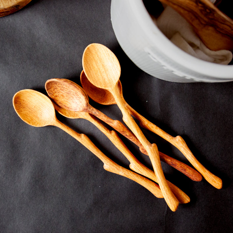 Pile of five wooden spoons with twig handles on a black background