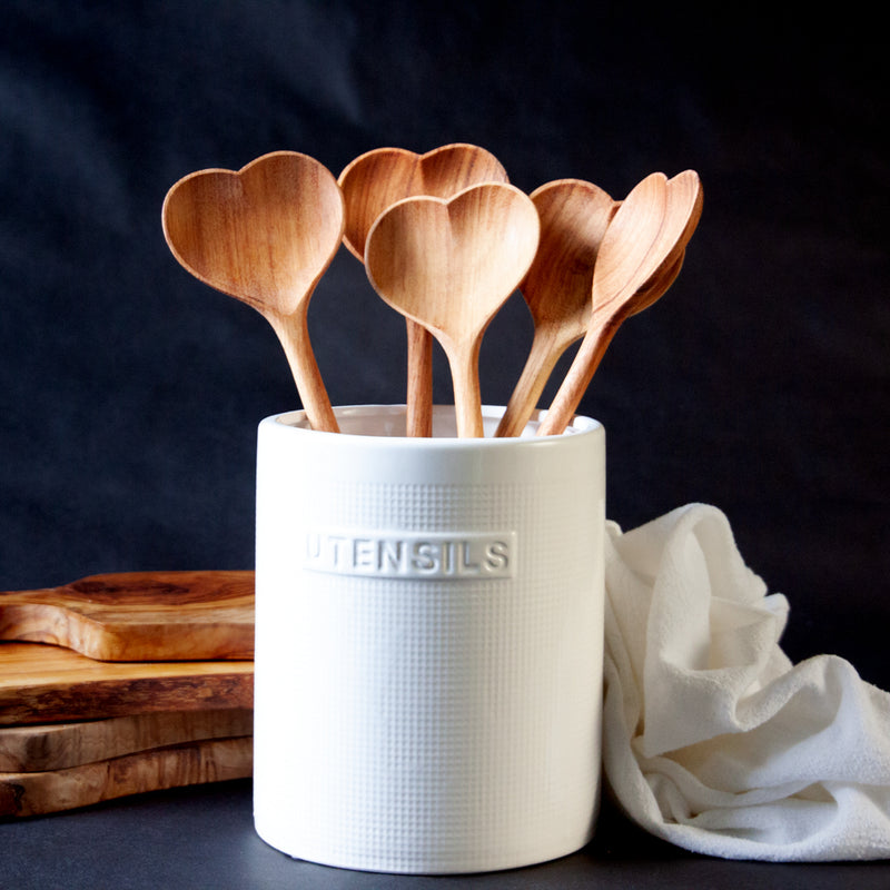 Five large heart shaped spoons in a white utensil crock on a black background