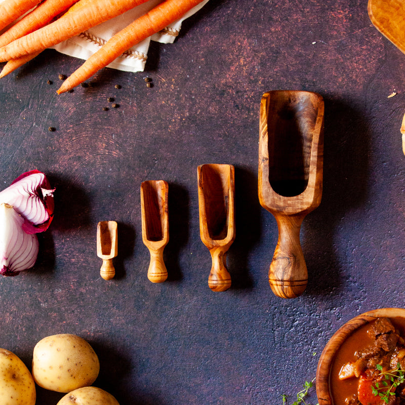 Four wooden scoop son dark background surrounded by ingredients for stew.