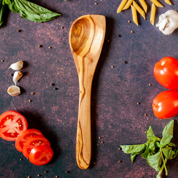 Wooden cooking spoon on dark rusty background surrounded by pasta ingredients