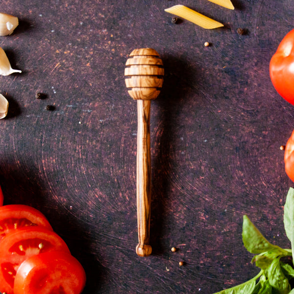Wooden honey dipper on dark rusty background with tomatoes, basil and peppercorns