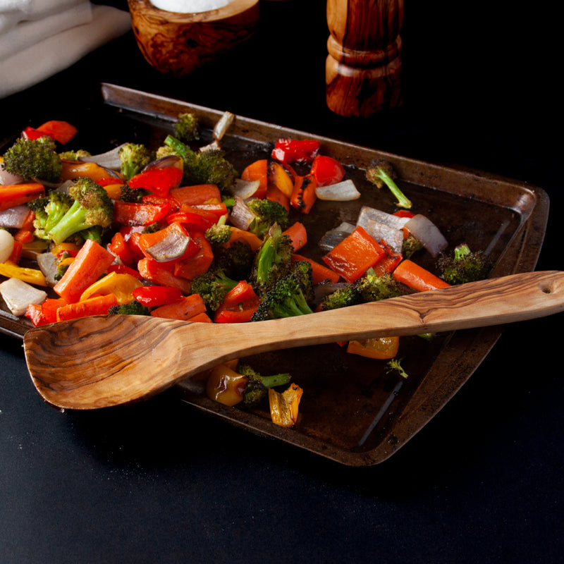Wooden kitchen spoon with a sheet pan of roasted veggies