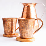 Copper mugs on wood coasters with a copper pitcher