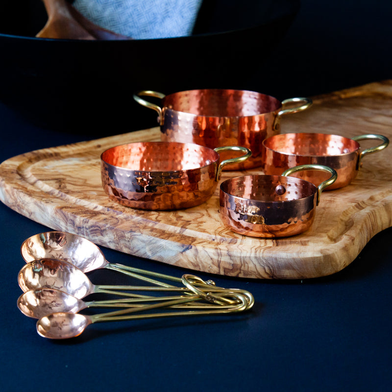 Copper and Gold Measuring Spoons and Cups on a wooden serving board and a dark background