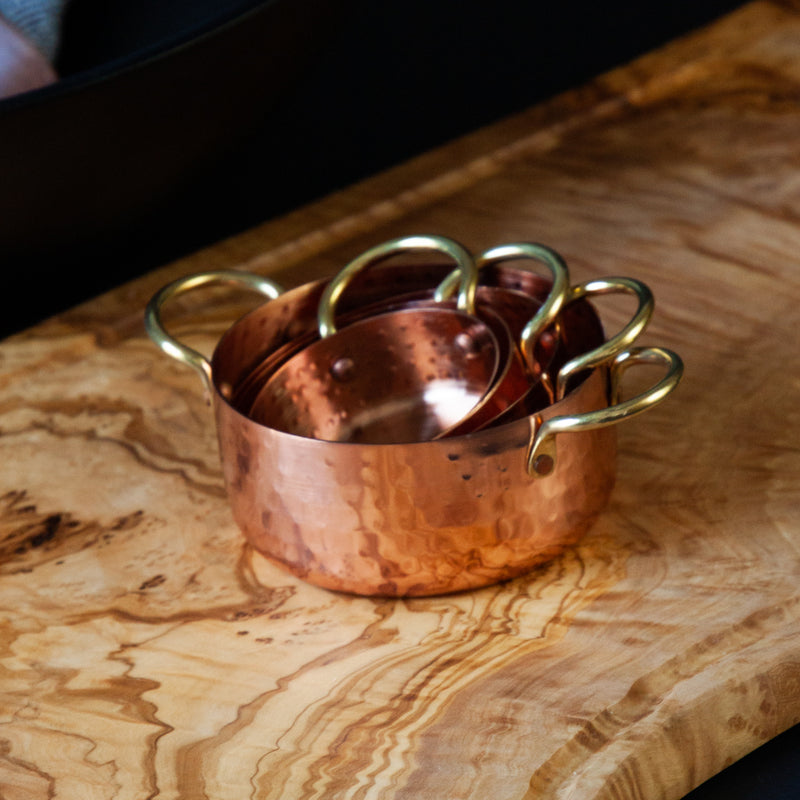 Set of 4 copper measuring cups stacked on a wood serving board