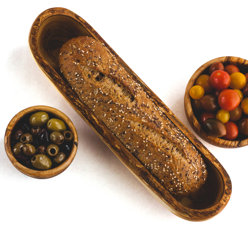 Loaf of bread in wooden dish, olives and tomatoes in wooden bowls