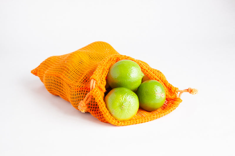 Green limes inside an orange produce bag