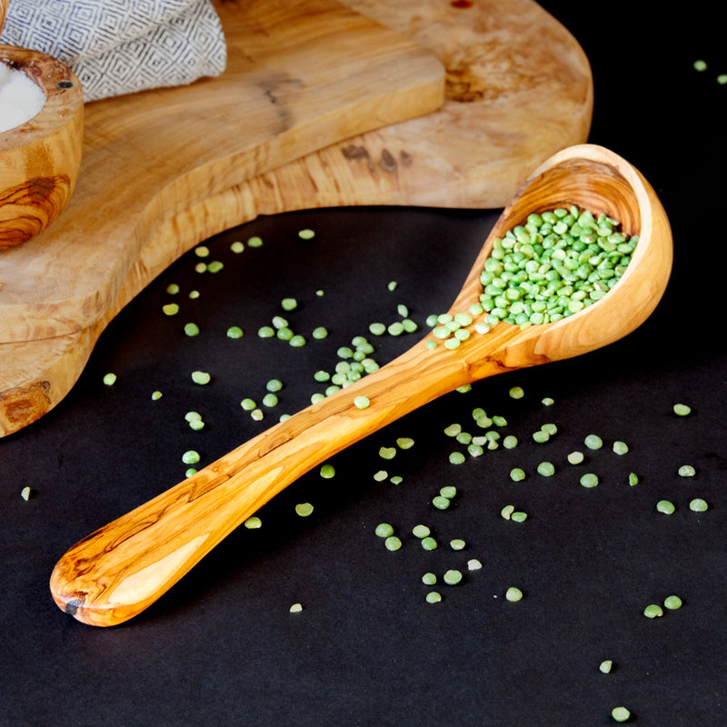 Wooden ladle with green split peas on a black surface with wood serving boards