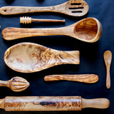 wood spoon rest surrounded by wooden kitchen utensils on a black surface